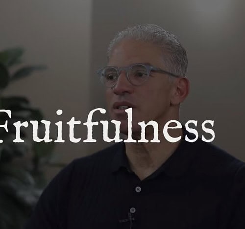dark overlay of a man seated in front of a plant talking off camera with the word fruitfulness over his face
